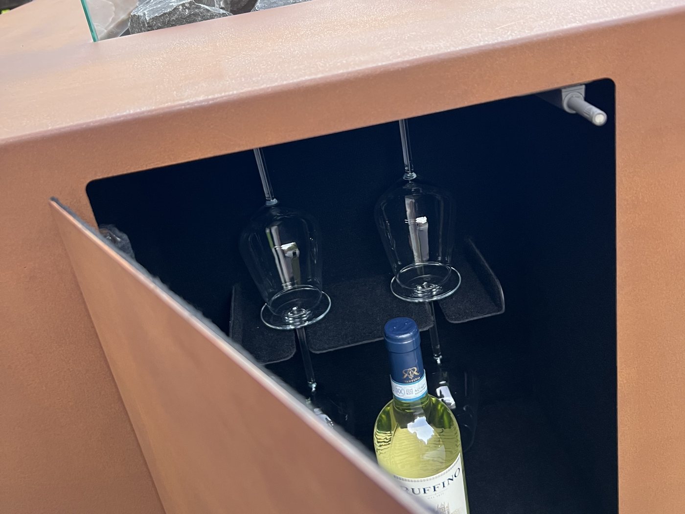 AGORA's open side compartment showing the glass holders and bottle storage, with the fire burning above