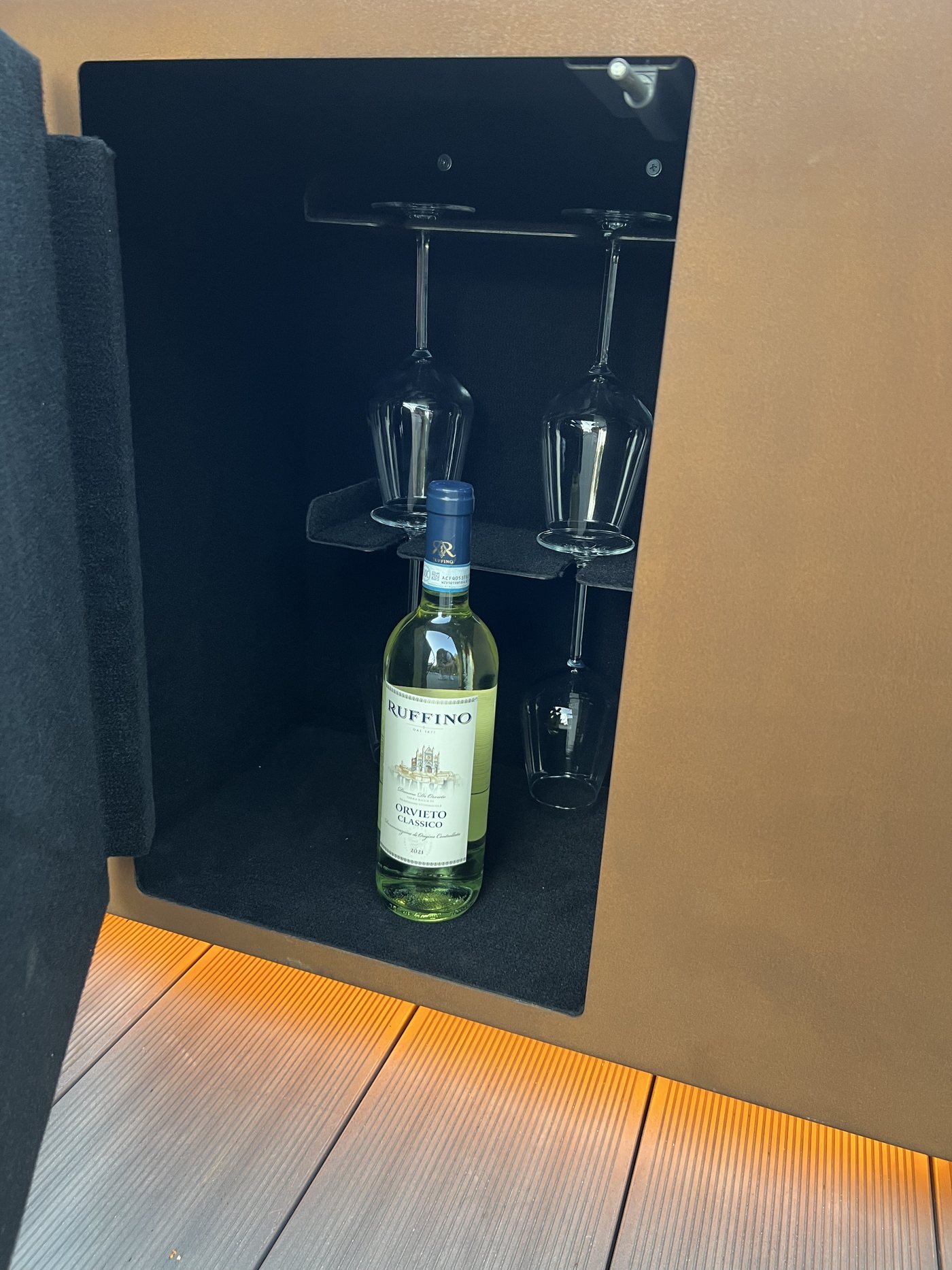 The built-in bar inside the AGORA body — a wine bottle cradled in the felt-lined compartment with two glasses in their holders