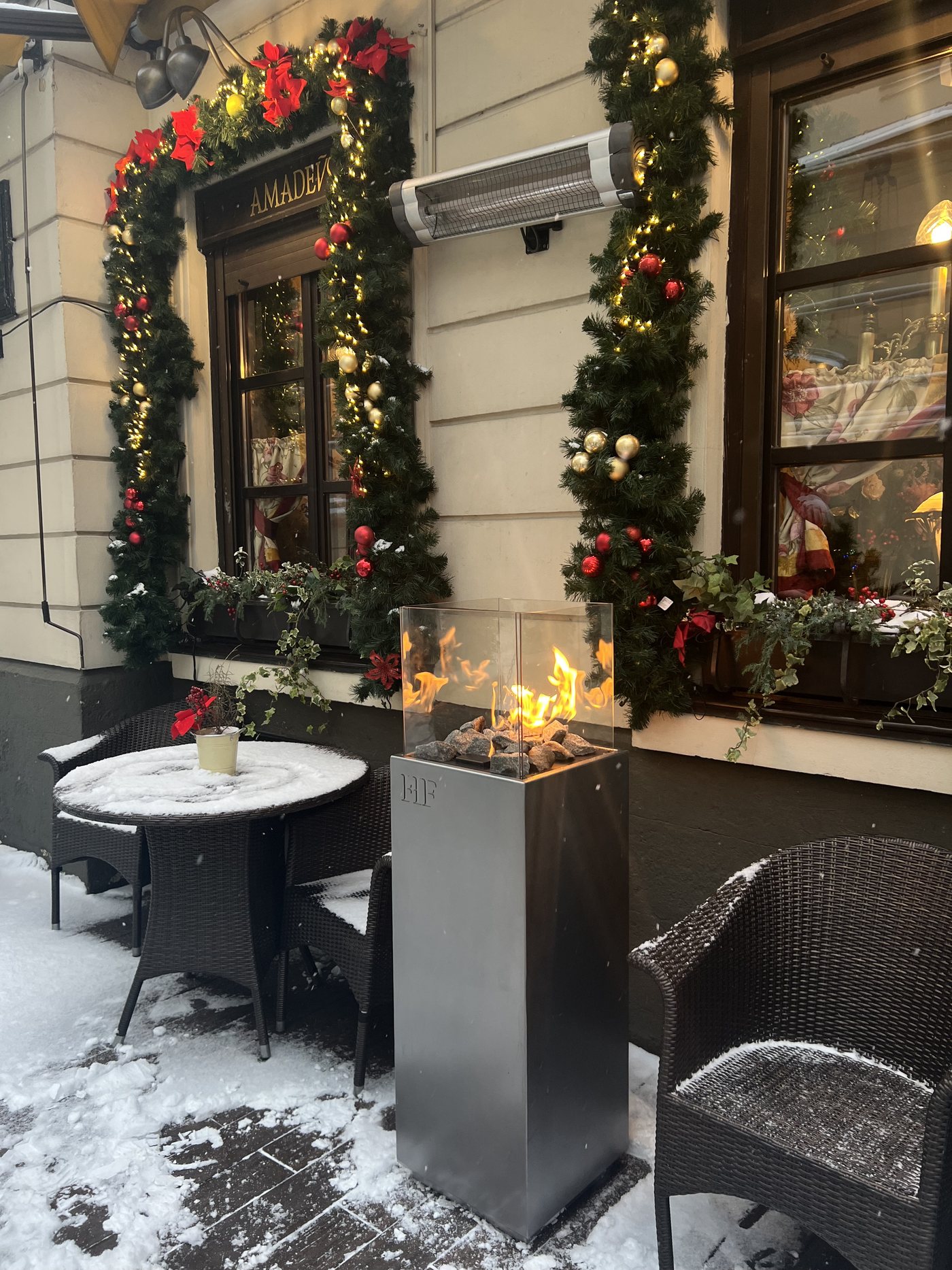 A RODOS fire column in graphite standing outside a restaurant facade in the snow, the HF monogram embossed on the body